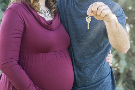 Pregnant Couple Happily Holds Our First Home Sign In Front Of Newly Purchased Home As New Homeowner