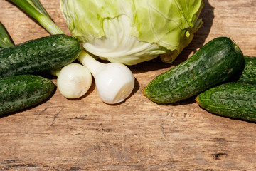 Fresh green vegetables on rustic wooden table. Cabbage, cucumbers and onion on wood table. Top view