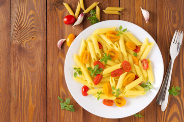 Penne pasta with yellow and red tomatoes decorated with basil on wooden background, low-calorie diet food, copy space