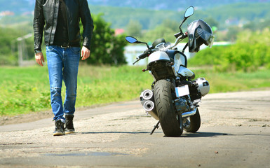 Fototapeta na wymiar Cool guy in leather jacket and jeans walks to his motorcycle