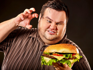 Diet failure of fat man eat fast food. Breakfast for mad overweight person who eating huge hamburger. Junk meal leads to obesity concept on black background. Feast for occasion. - 207671323