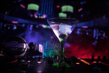 Glass with martini with olive inside on dj controller in night club. Dj Console with club drink at music party in nightclub with disco lights. Close up view