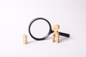 A wooden figure of a woman and a child stands near the magnifying glass. The concept of finding a child, the adoption of children. Mother lost her baby and is now looking for him.