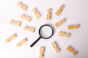 Wooden figures of people lie around a magnifying glass on a white background. The concept of the search for people and workers, human resources. Hiring for work, tracing people.