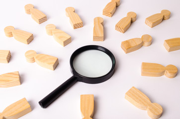 Wooden figures of people lie around a magnifying glass on a white background. The concept of the search for people and workers, human resources. Hiring for work, tracing people.