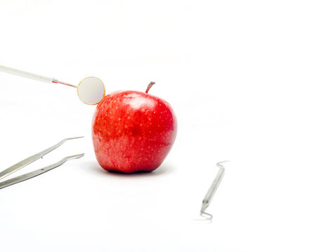 Dental mirror and probe and tweezer with fresh apple isolated in white background