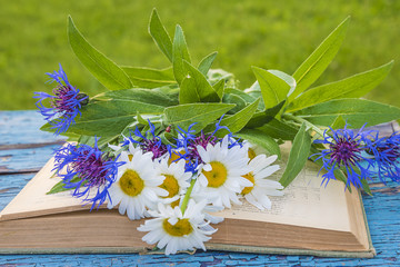 Bunch of white daisies and blue cornflowers on old book and rustic wooden background outdoors