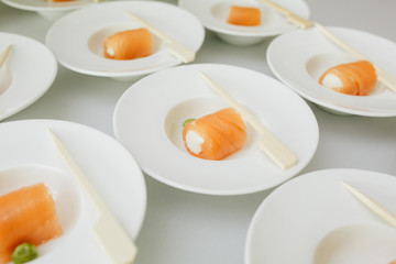 delicious salmon rolls with cream cheese on white plates in the form of a cold snack for guests.