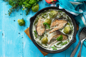 Red fish and vegetables baked (brussels sprouts, green beans) in cream sauce in a frying pan in a rustic style. Top view flat lay background.