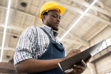 Waist-up portrait of concentrated African American technician wearing checked shirt and overall...