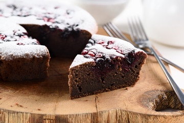 Homemade chocolate berry cake with bird cherry flour. Piece of bird cherry cake in icing sugar on oak board
