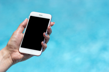 Hand of a young girl holding a smartphone near the pool