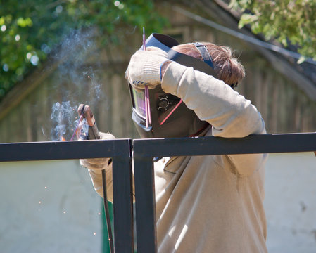 Male welder mounts the fence. Man in protective mask