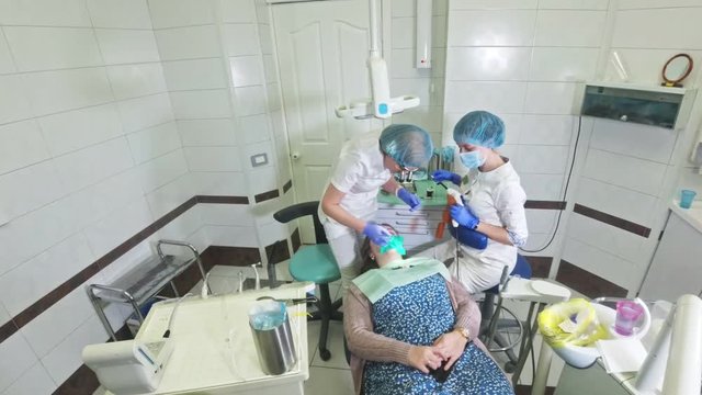 Woman at dentist clinic gets dental treatment to fill a cavity in a tooth. Dental restoration and composite material polymerization with UV light and laser. Shooting at a wide angle.