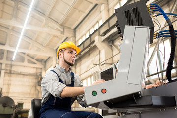 Portrait shot of bearded operator wearing protective helmet sitting in front of CNC machine and...