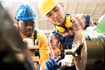 Multi-ethnic team of lathe operators wearing overalls and hardhats gathered together at production...