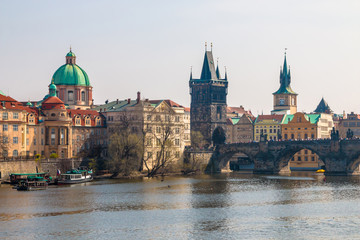 Fototapeta premium Charles Bridge, Old Town Bridge Tower and St Francis Of Assisi Church in a scenic view from Vltava river with cruise boats in Prague, Czech Republic
