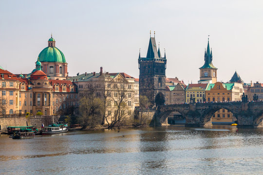 Charles Bridge, Old Town Bridge Tower and St Francis Of Assisi Church in a scenic view from Vltava river with cruise boats in Prague, Czech Republic