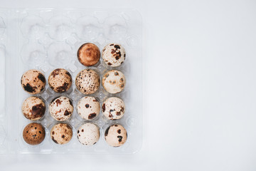 Uncooked scattered quail eggs in transparent box on white background