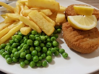 Tasty lunch in English style - fish cakes, chips, peas on a white plate