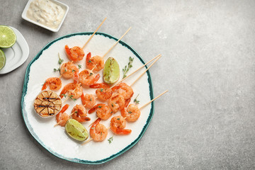 Plate with delicious fried shrimp skewers and lime on grey background, top view