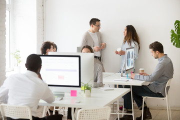 Obraz premium Multiracial workers working in coworking space, doing different things, colleagues chatting and casual talking, employees developing schedules at pc, analyzing financial graphs. Cooperation concept