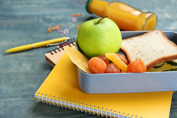 Lunch box with appetizing food and stationery on table
