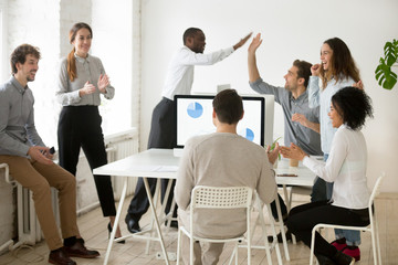 Excited multiracial team laughing celebrating shared goal achievement, successful startup project, greeting with online win, staff giving high fives for common business victory in coworking space