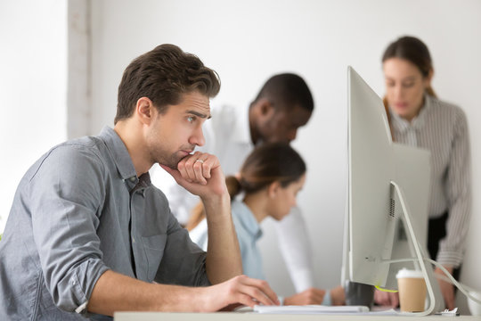Thoughtful male employee looking at screen browsing web, surfing internet reading financial news at desktop computer, focused worker busy working at pc, analyzing reports and statistics online