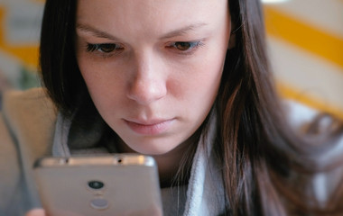 Young seriously woman reading something on her mobile phone sitting in cafe. Closeup face.