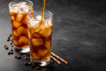 Ice coffee in a tall glass over and coffee beans on a old rustic wooden table. Cold summer drink on a dark background with copy space. The process of pouring drink from a coffee pot into a glass