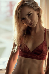 Beautiful blonde woman dressed in lace lingerie sitting against window on background. Concept of tenderness. Sensual portrait.