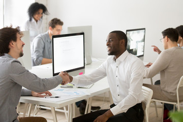 African American worker and Caucasian business client laughing shaking hands, congratulating with successful company contract, making good first impression, greeting at workplace