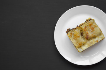 Traditional italian beef lasagne on a white round plate on black background, top view. Flat lay. From above. Copy space and text area.