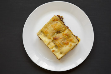 Traditional beef lasagne on a white round plate on black background, top view. Flat lay. From above.