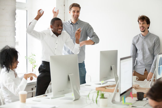 Positive multiracial team having fun together, laughing and throwing paper balls, diverse colleagues enjoy spending work break, playing childish at workplace. Concept of teambuilding, good relations