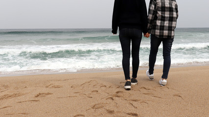 The back of two women standing on the beach.