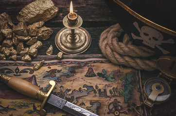 Fototapeta na wymiar Pirate treasure map, gold nuggets, dagger and pirate hat on aged wooden table background. Sea travel.