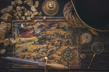 Pirate treasure map, gold nuggets, dagger and pirate hat on aged wooden table background. Sea travel.