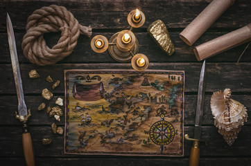 Treasure map, gold nugget, dagger sword, rope and seashell on wooden table background.