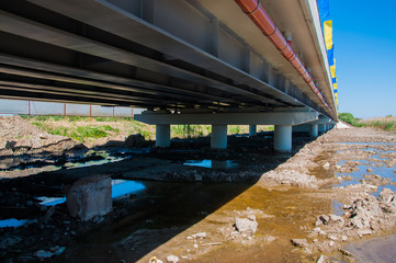 Down view of a construction of a bridge with concrete columns. Mud and water under it