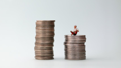 A miniature man sitting on a pile of low coins.