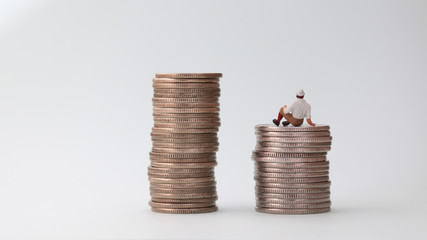 The back of miniature man sitting on coins.