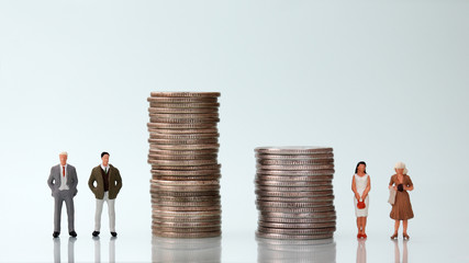 The concept of gender pay discrimination. Two pile of coins and four miniature people.