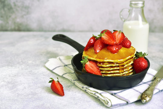 Homemade delicious pancakes with maple syrup and fresh ripe strawberry in a skillet pan.