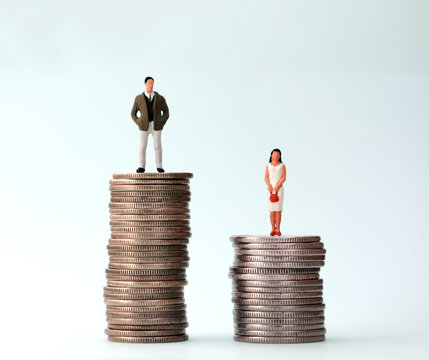 A miniature man and a miniature woman standing on a pile of coins at different heights.