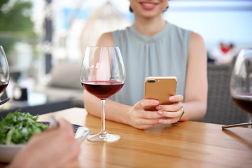 Young woman with smartphone and glass of wine at table