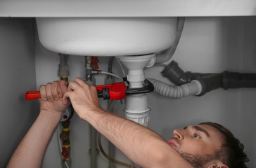 Professional plumber fixing sink with pipe wrench, closeup