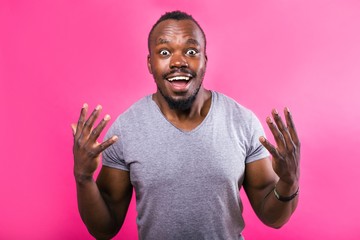 Emotional African man raised his hands on pink background