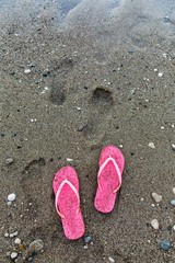 Pink flip flop on the beach with footprints in the sand